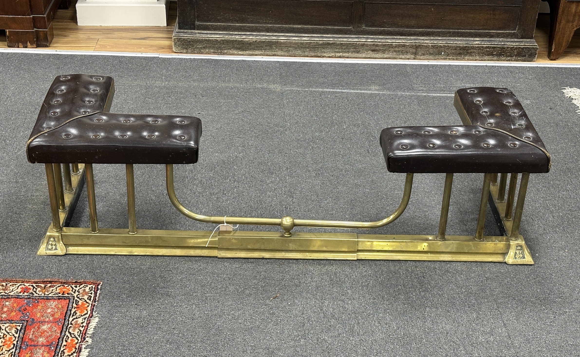 An early 20th century brass and buttoned brown leather telescopic club fender, minimum width 132cm, depth 40cm, height 36cm